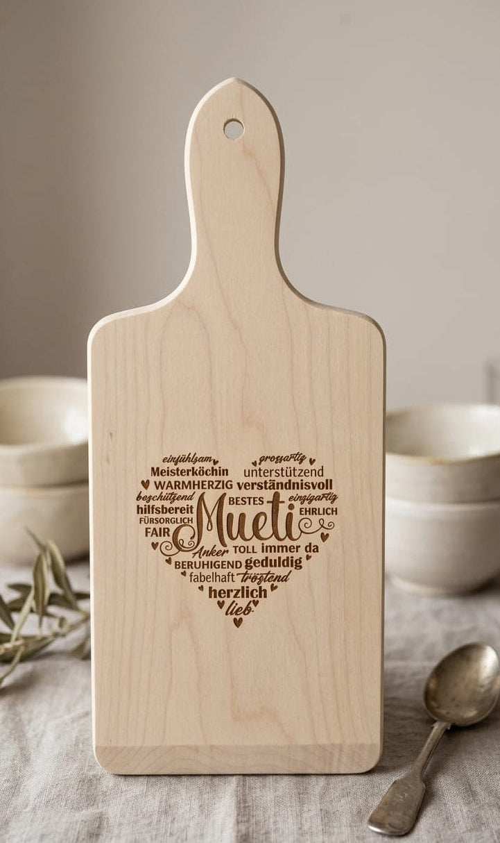 Personalisiertes Holzschneidebrett für 'Mueti' mit Lasergravur in Herzform. Geschenkidee aus hellem Holz mit liebevollen Begriffen wie 'Meisterköchin', 'Lieblingsmensch' und 'Herzlich'.